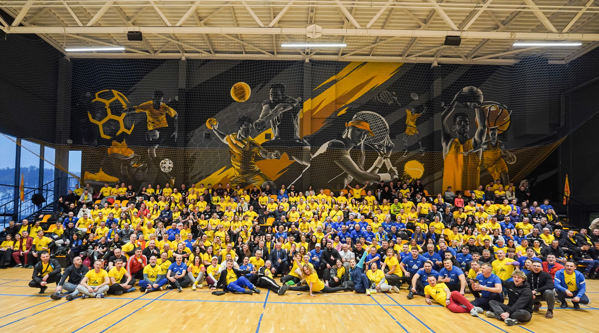 Велика група дітей та дорослих у спортивній залі, всі в яскравих жовтих та синіх футболках