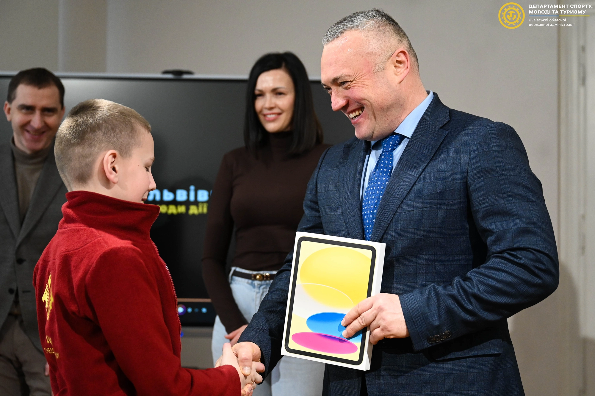 Чоловік у костюмі вручає нагороду хлопчику, поруч стоять усміхнені дорослі в офіційній обстановці