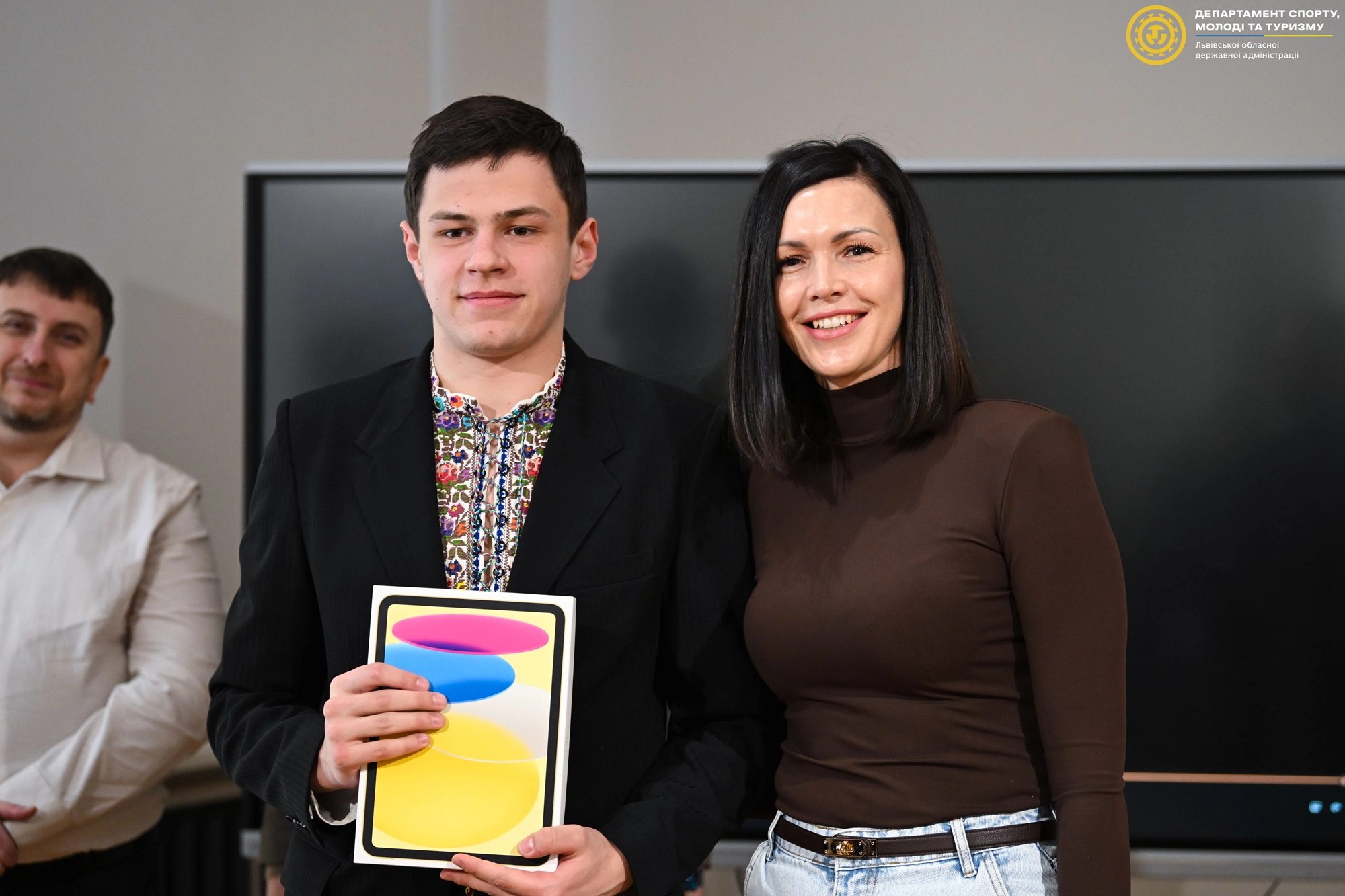 Чоловік у вишиванці тримає нагороду, поруч жінка усміхається, на фоні екран телевізора