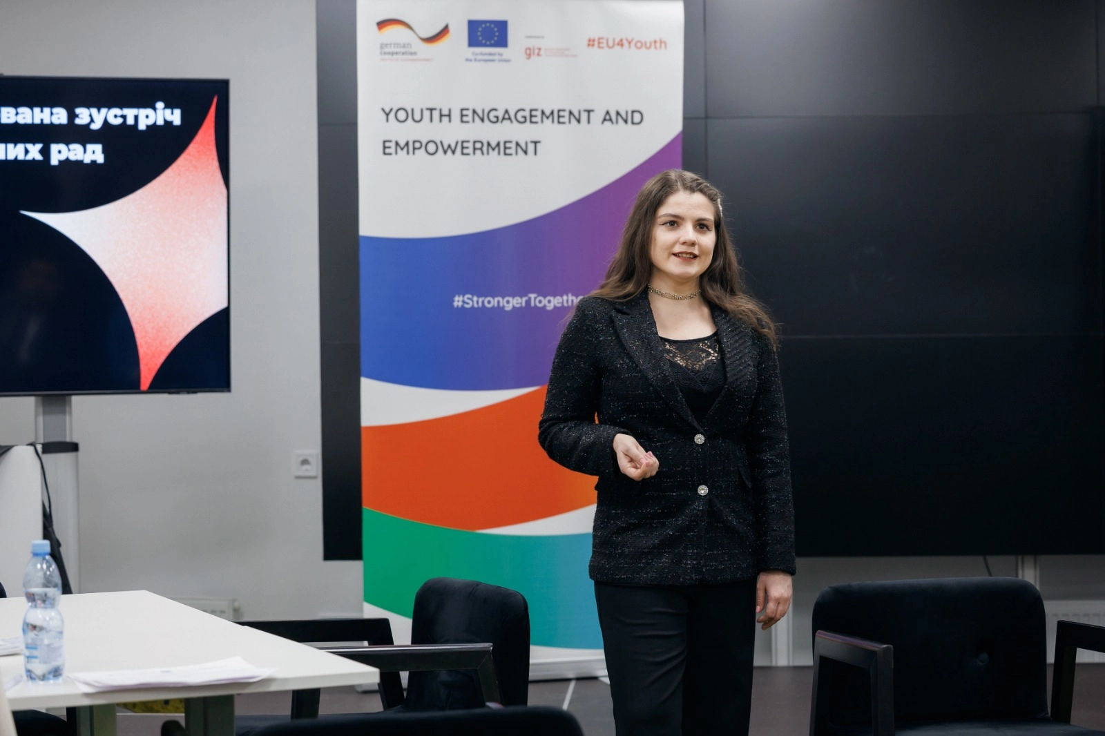 Жінка виступає на фасилітованій зустрічі молодіжних рад у Києві, на задньому плані банер EU4Youth